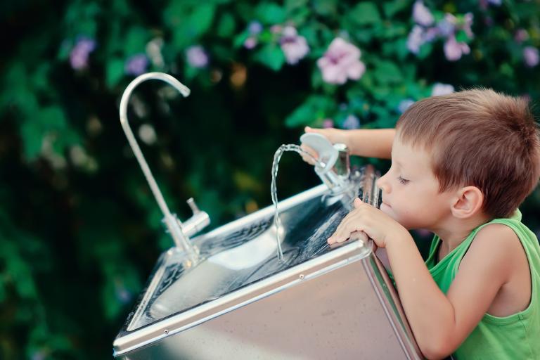 a young boy drinking from a water bubbler fountain in the park